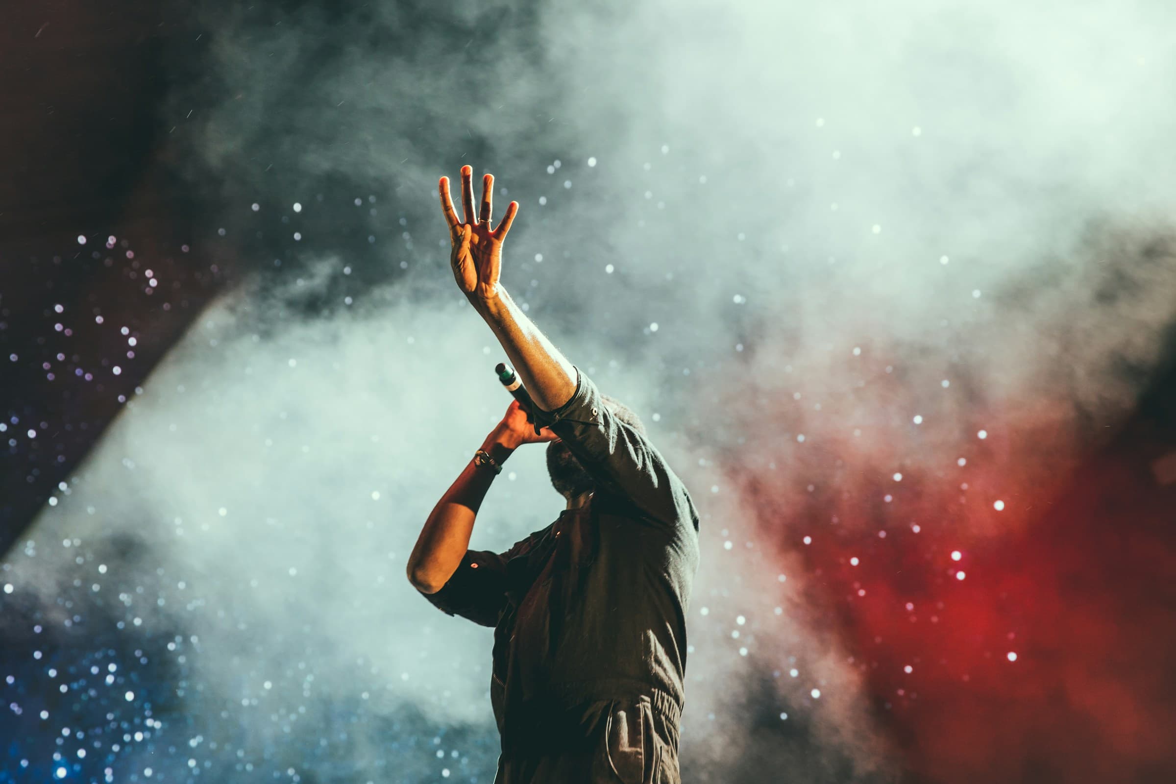 Silhouette on stage, hand raised into smoke and stage light