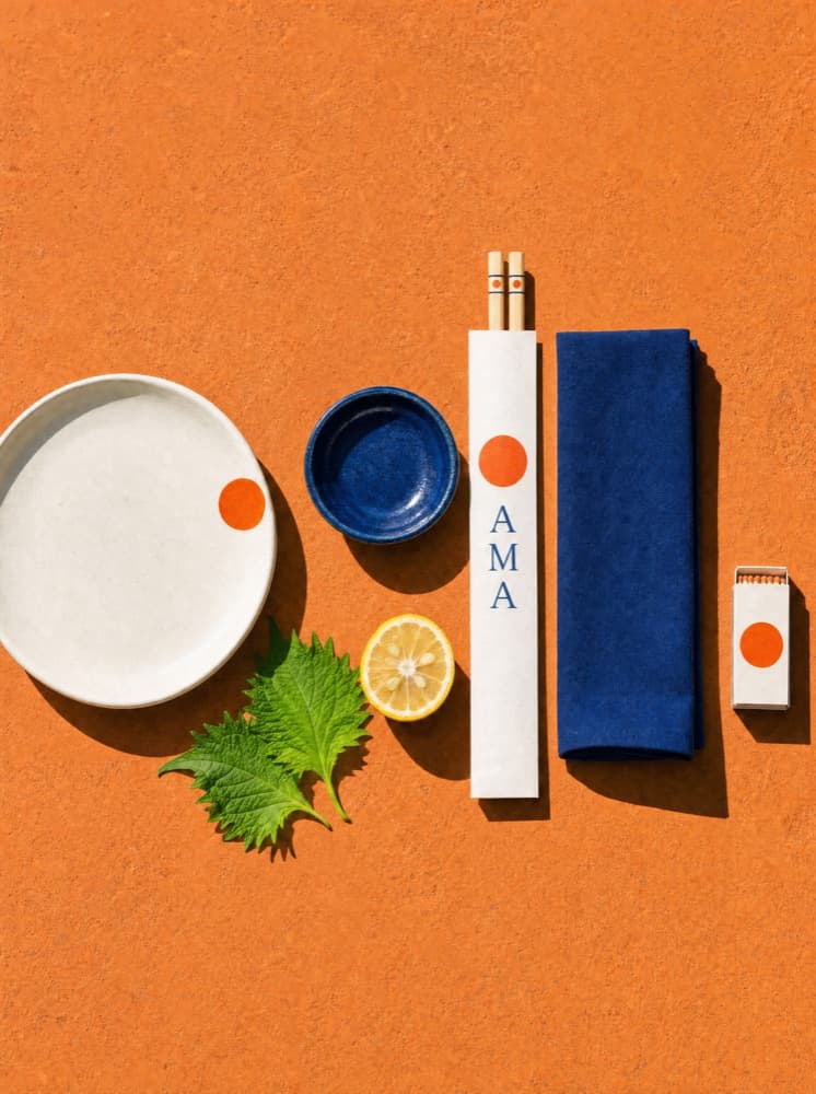 The place setting from above: off-white plate, cobalt dipping dish, chopsticks in a printed paper sleeve, indigo napkin, matchbook, shiso and half a lemon